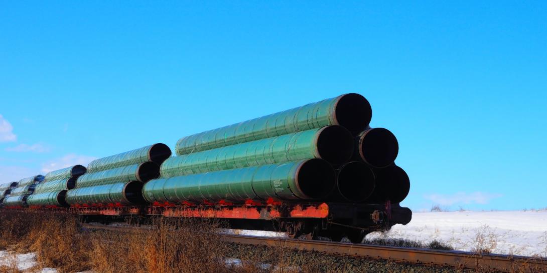 Image of pipeline pieces traveling on train tracks against a blue sky
