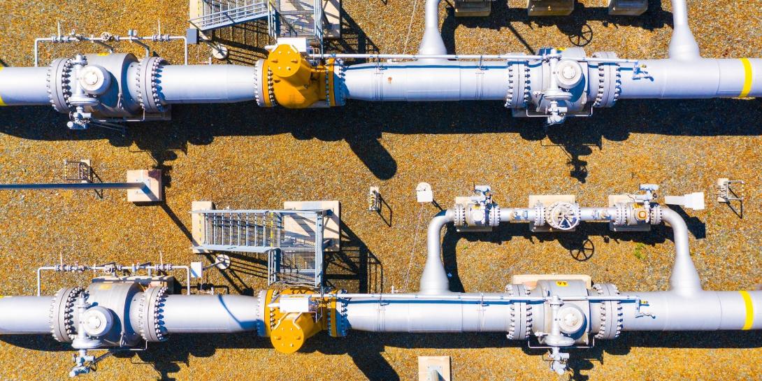 Overhead photo of two narrow white natural gas pipelines on a tan surface